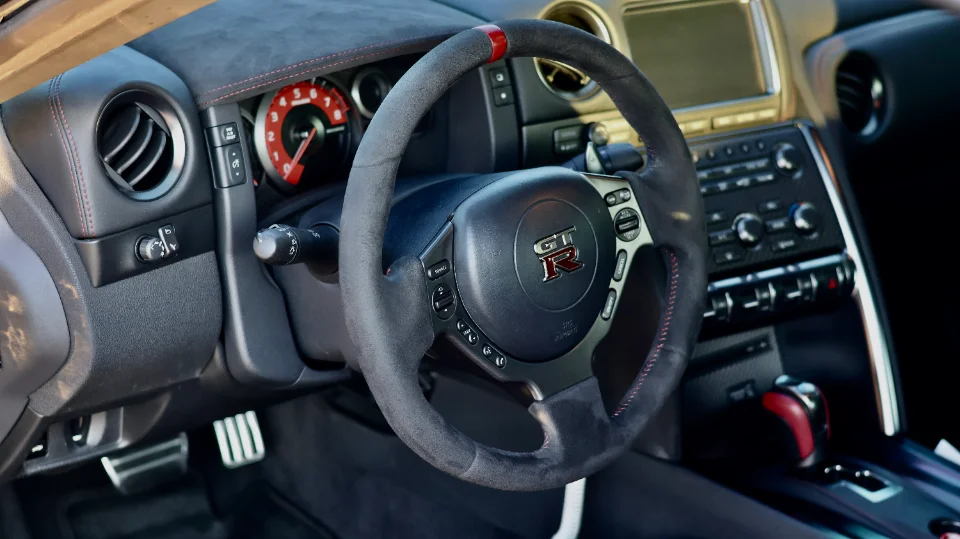 Detailed interior shot of a Nissan GT-R featuring an Alcantara steering wheel with red stitching and dashboard.