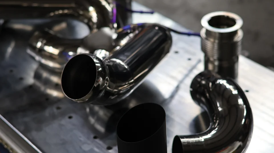 Close-up of polished stainless steel exhaust pipes and a black exhaust tip for a performance vehicle, laid on a metal surface.