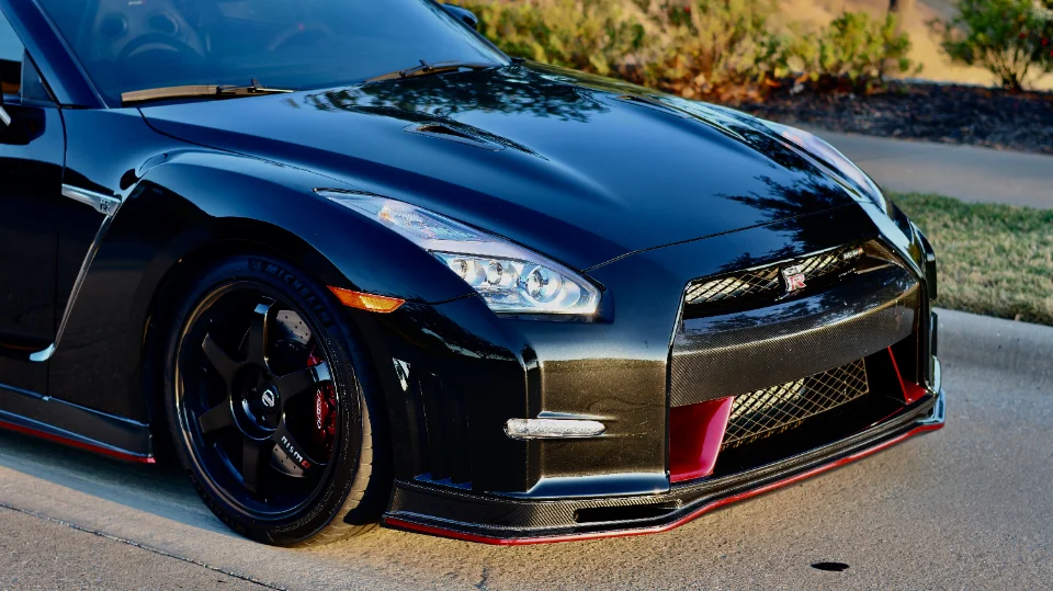 A close-up of a black Nissan GT-R showcasing its carbon fiber front splitter, grille, and aftermarket wheels with red brake calipers.