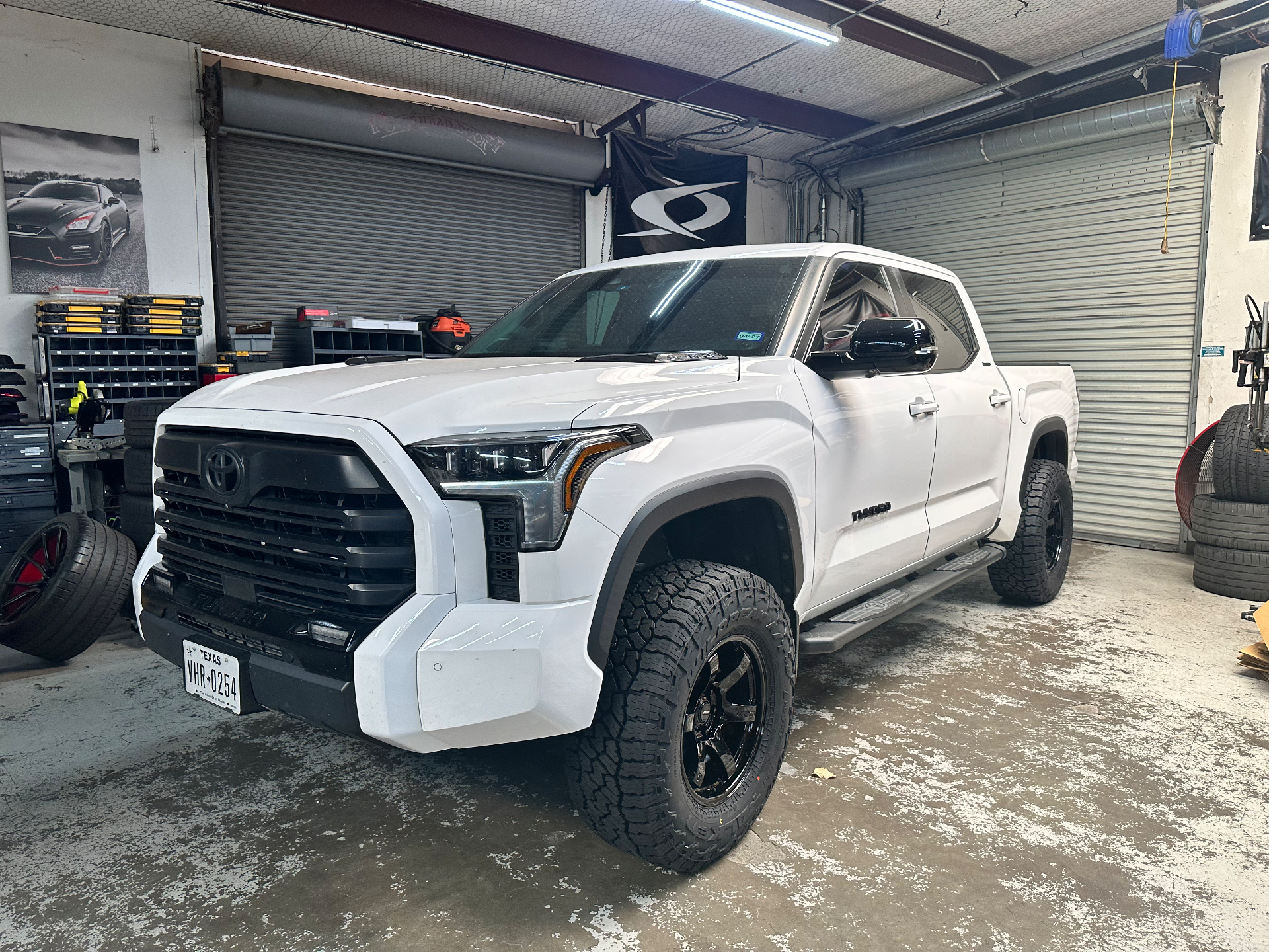 A white Toyota Tundra truck with aftermarket wheels and off-road tires parked inside a garage.