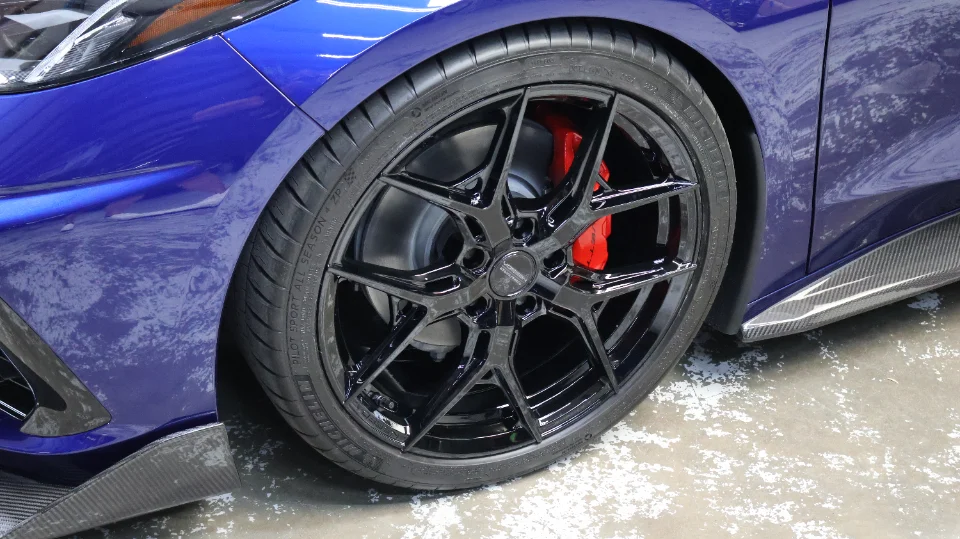 Close-up of a blue Corvette C8 with black aftermarket wheels, red brake calipers, and carbon fiber side skirts.
