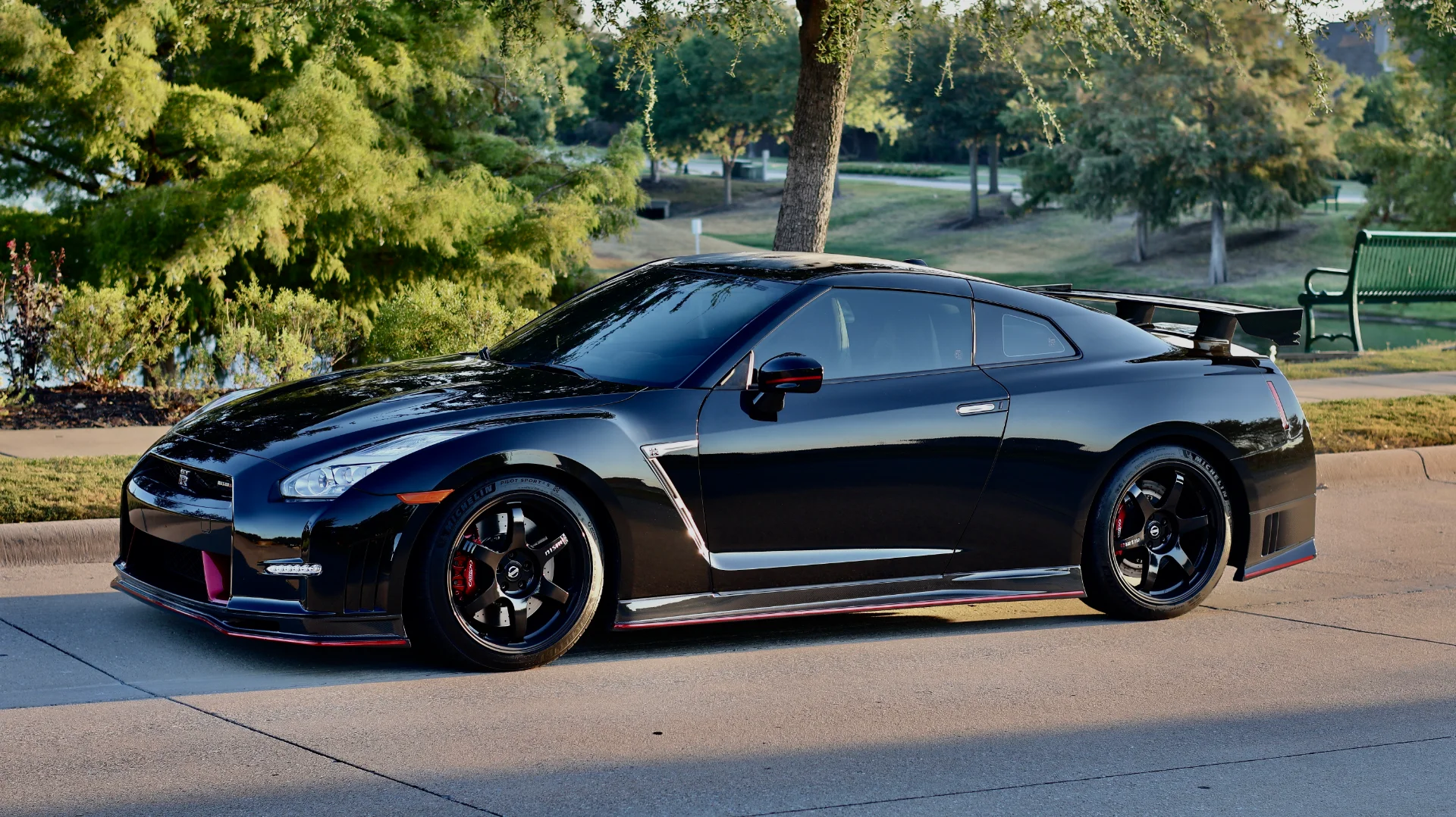 A black Nissan GT-R R35 with aftermarket wheels and a large rear wing parked on a sunny day.