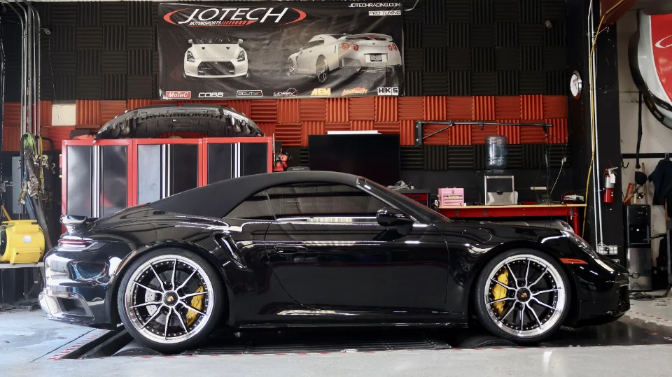 A black Porsche 911 convertible strapped to a dynamometer at Jotech Motorsports for performance tuning.