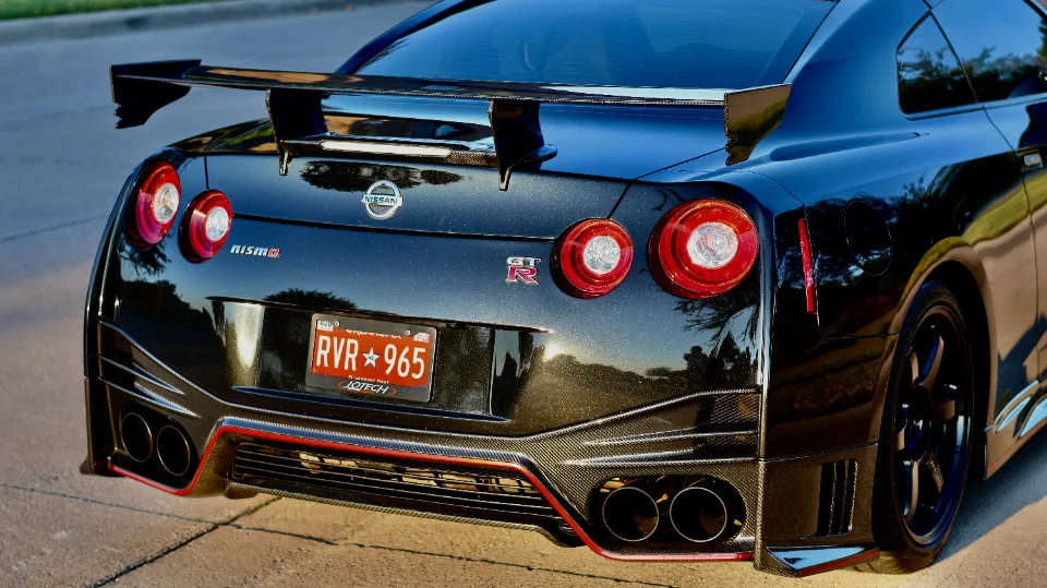 A black Nissan GT-R R35 with a large carbon fiber wing, custom rear diffuser, and aftermarket quad exhaust tips.