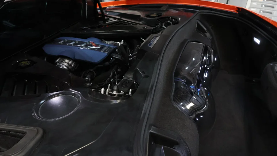 Close-up view of a C8 Corvette engine bay with a blue aftermarket intake manifold and carbon fiber components.