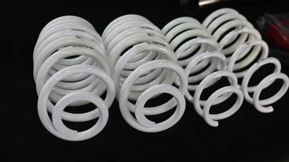 Close-up of white performance suspension springs for a car, neatly arranged on a dark background.
