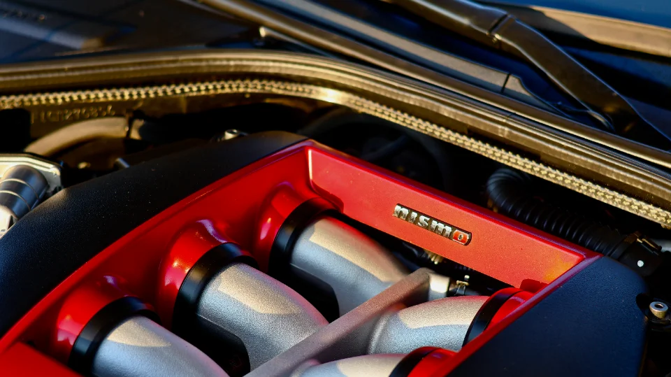 A close-up view of a red Nismo intake manifold in a Nissan GT-R engine bay, showcasing the engine's details.