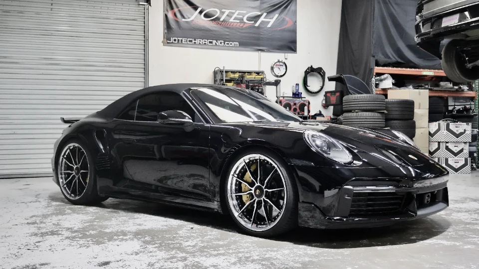 A black Porsche 911 with custom multi-spoke wheels and gold brake calipers parked inside the Jotech Motorsports shop.