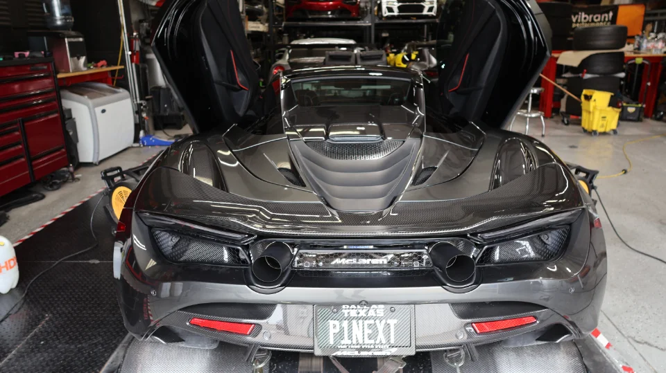 A McLaren 720S with its butterfly doors open, strapped to a dynamometer in a performance tuning shop.