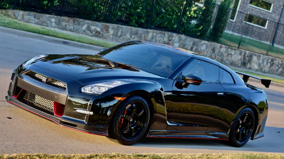 A black Nissan GT-R with aftermarket wheels and carbon fiber aerodynamic parts parked on a street.