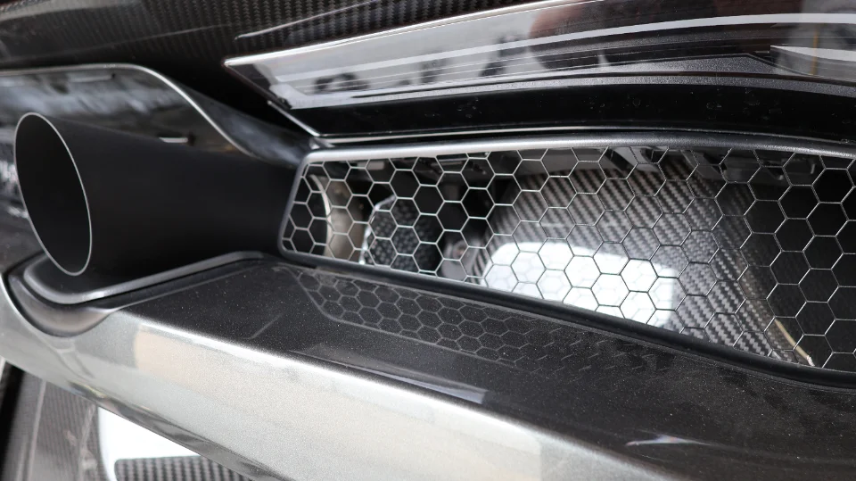 A close-up detail of a car's black exhaust tip, carbon fiber rear diffuser, and honeycomb grille.