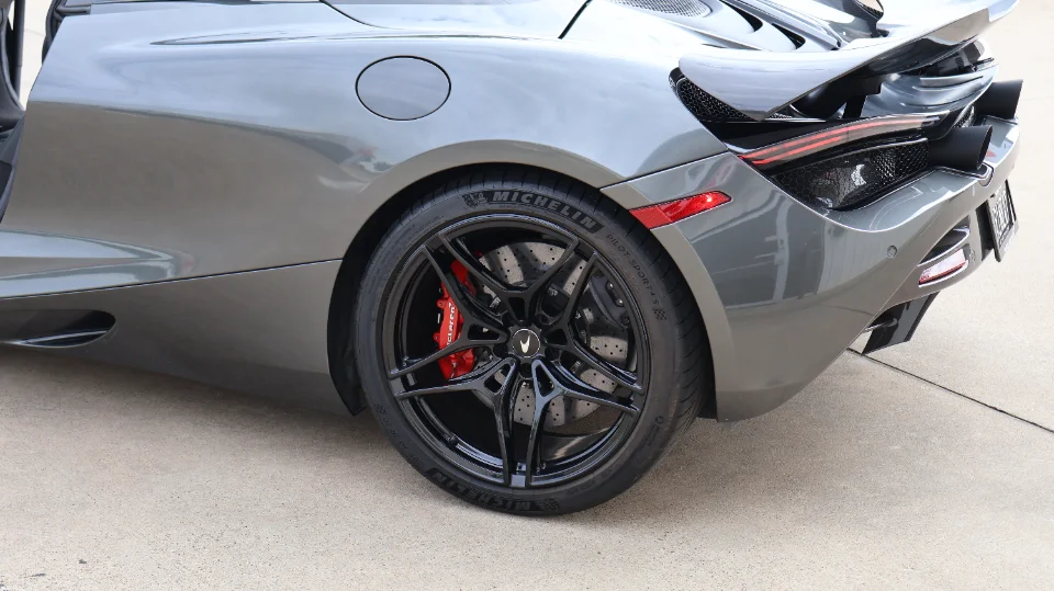 A grey McLaren 720S rear wheel with black multi-spoke rims, red brake calipers, and Michelin tires.