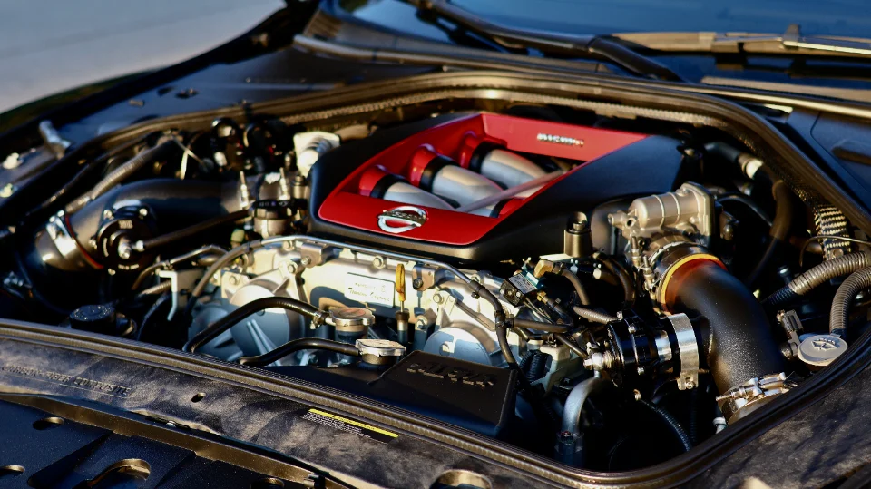 A close-up view of a Nissan GT-R VR38DETT engine bay featuring a red aftermarket intake manifold and performance induction system.