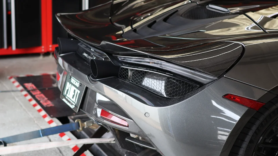 Rear view of a grey McLaren supercar strapped to a dynamometer, showcasing its carbon fiber aero and exhaust.
