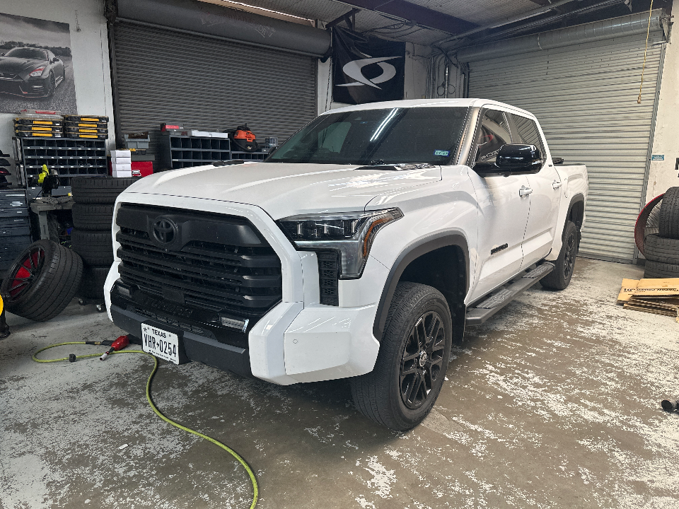 A white Toyota Tundra truck parked inside a garage or shop with a Texas license plate.