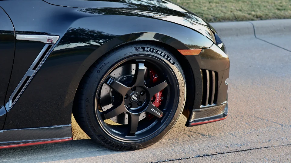Close-up of a black Nissan GT-R's front wheel, featuring Nismo wheels, Michelin tires, and red Nismo brake calipers.