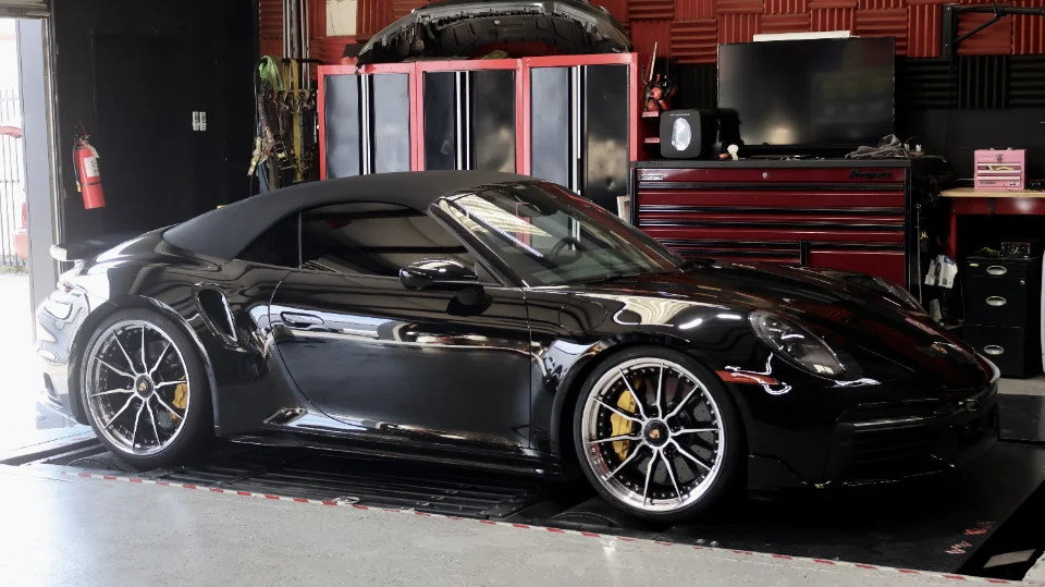 A black Porsche 911 convertible on a dynamometer in a performance tuning shop.