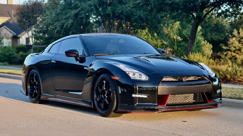 A black Nissan GT-R with aftermarket wheels and a rear spoiler parked on a residential street.