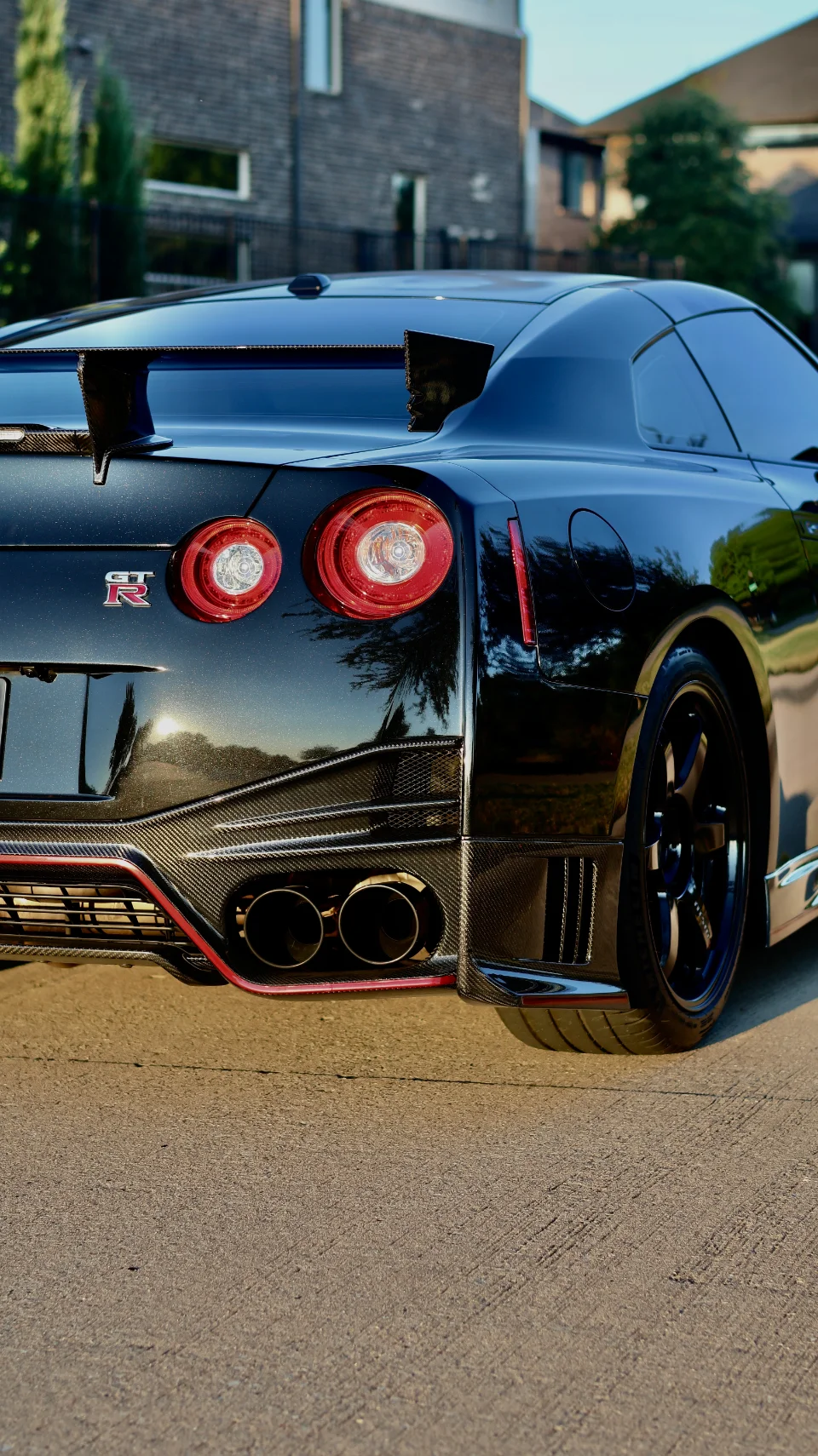 A black Nissan GT-R R35 from the rear, showcasing a carbon fiber diffuser, large rear wing, and aftermarket exhaust.