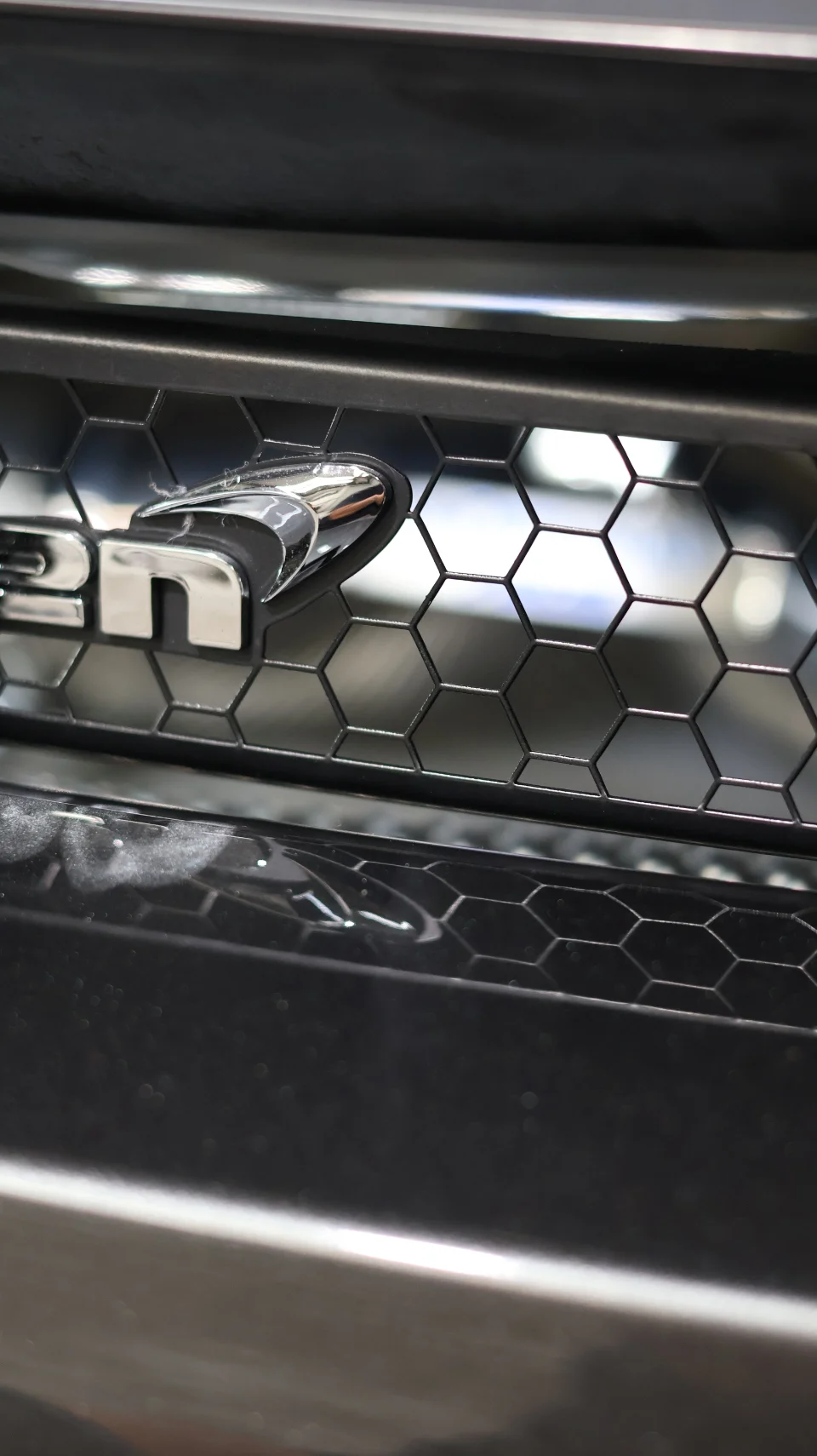 Close-up detail of a McLaren's front grille with honeycomb pattern and chrome badge, showcasing the car's design.