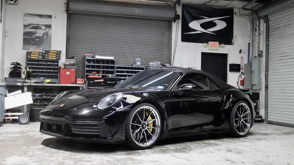 A black Porsche 911 convertible with custom multi-spoke wheels and yellow brake calipers parked in a clean garage.