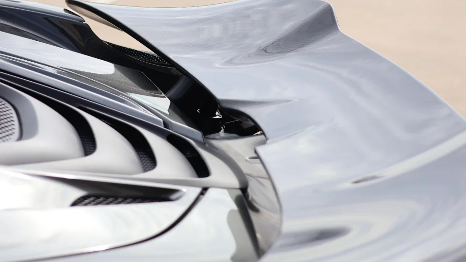 Close-up detail of a grey supercar's rear wing and intricate bodywork, highlighting aerodynamic features and vents.