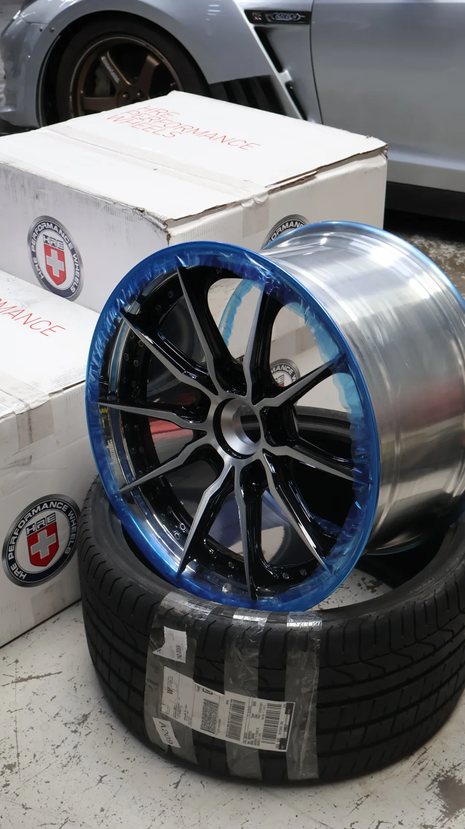New HRE Performance wheels and tires in their packaging, ready for installation on a Nissan GT-R at a performance shop.