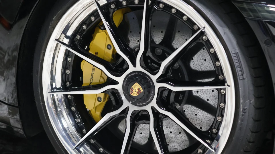 Close-up of a Porsche wheel with multi-spoke black and white custom wheels, yellow brake calipers, and Pirelli tires.