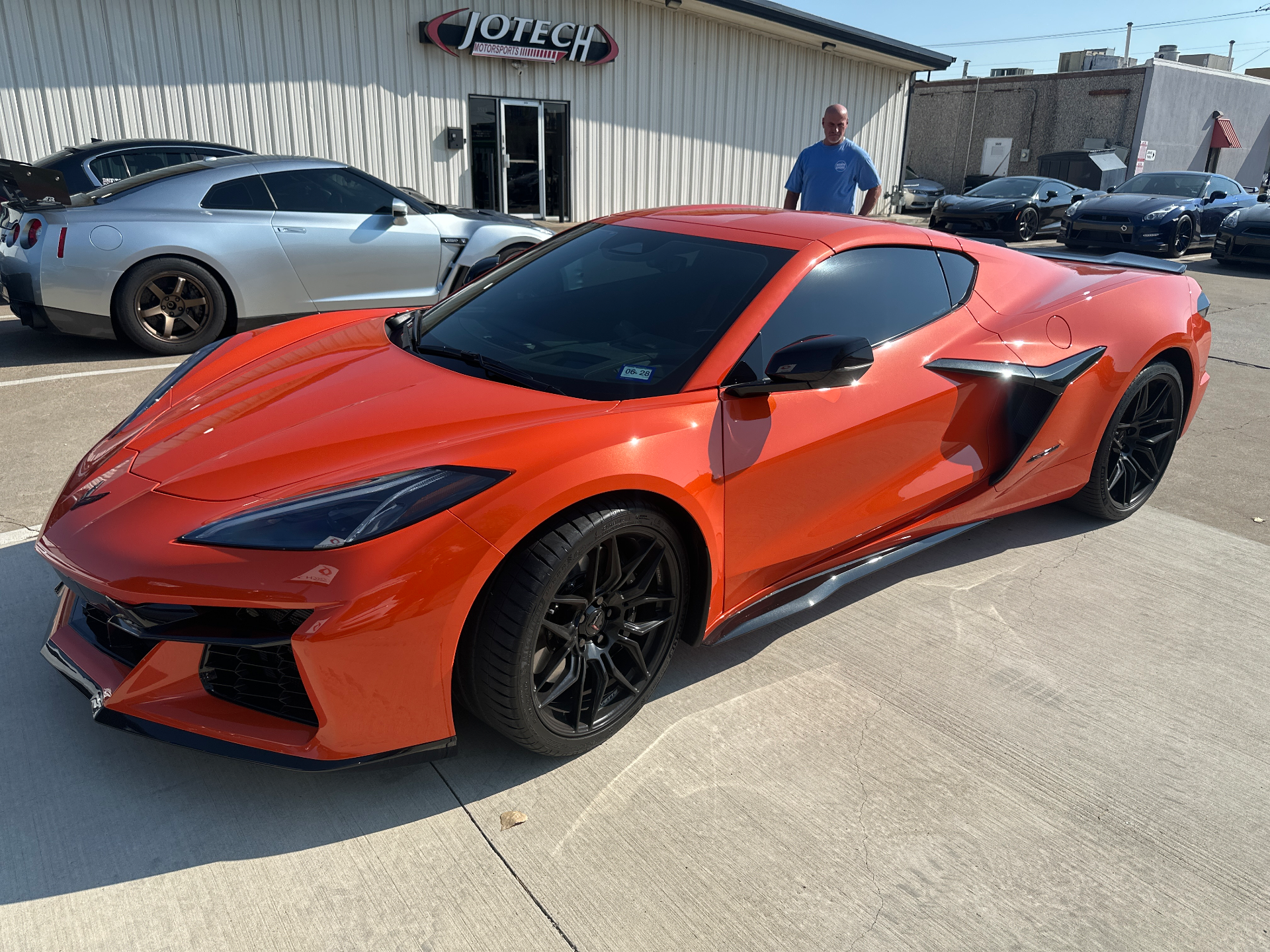 An orange Corvette C8 and a silver Nissan GT-R parked outside Jotech Motorsports performance tuning shop.