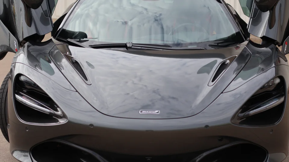 Front view of a grey McLaren 720S with its butterfly doors open, showcasing its sleek design.