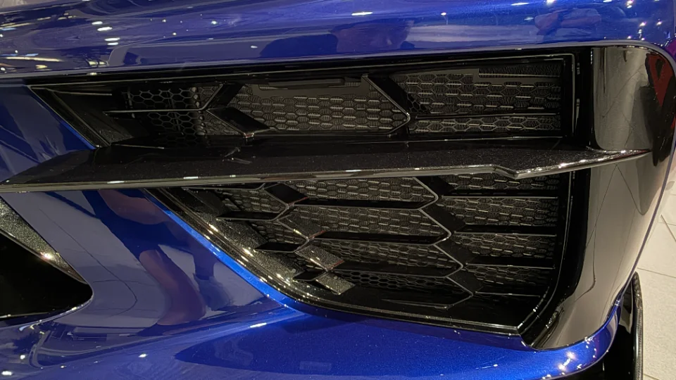 Close-up detail of a blue car's front bumper and honeycomb grille with a glossy finish.