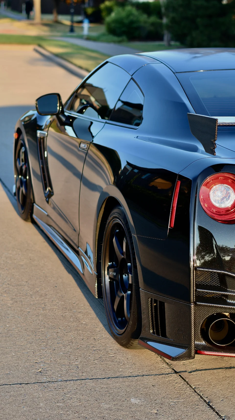 A black Nissan GT-R with aftermarket wheels and carbon fiber aero parked on a street.