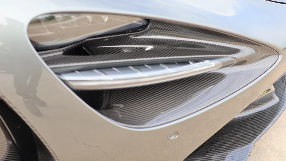 Close-up of a supercar's carbon fiber fender vent and bodywork, highlighting intricate details.