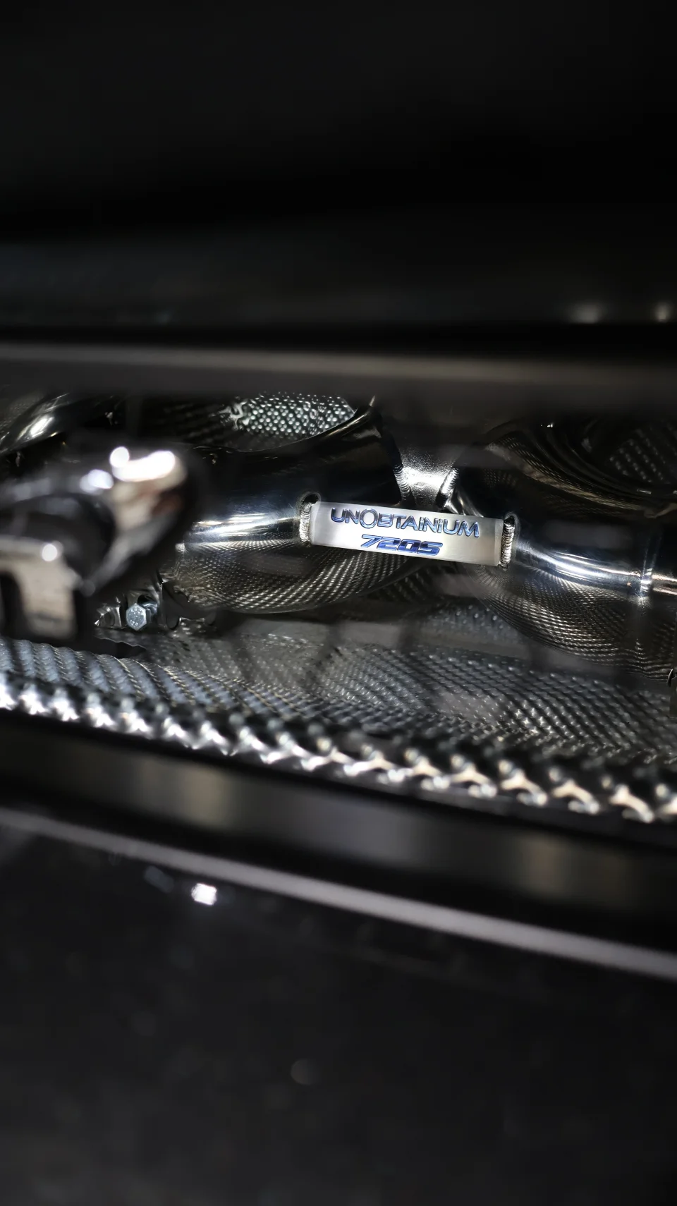 Close-up detail of an Unobtainium exhaust component with carbon fiber heat shielding on a McLaren 720S.