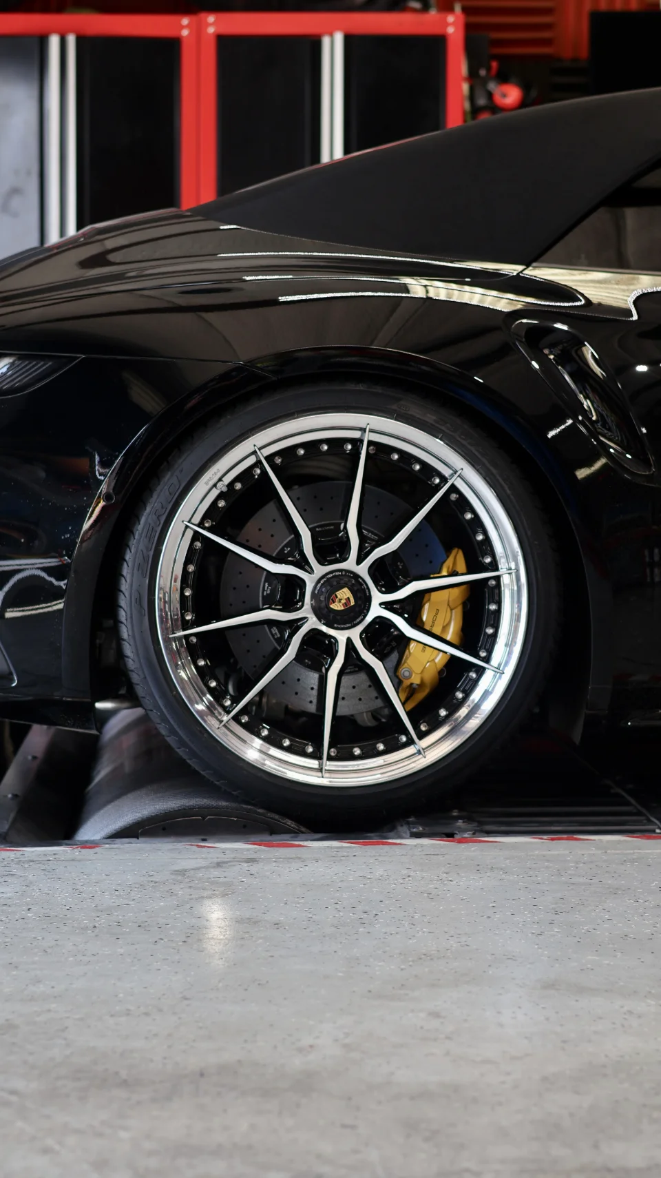 Close-up of a black Porsche on a dyno, showcasing custom multi-spoke wheels and yellow brake calipers.