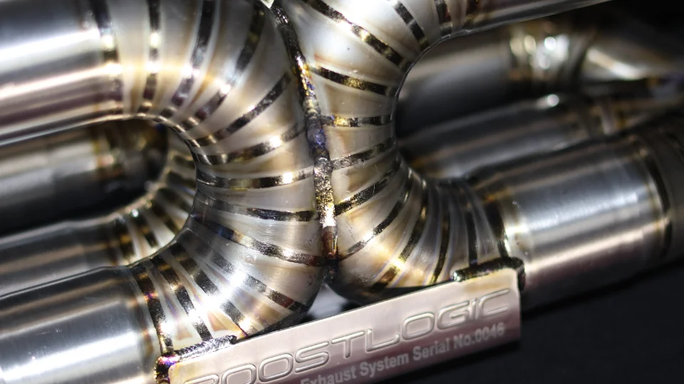 Close-up of a BoostLogic titanium exhaust system with intricate welds and piping, showcasing the craftsmanship.