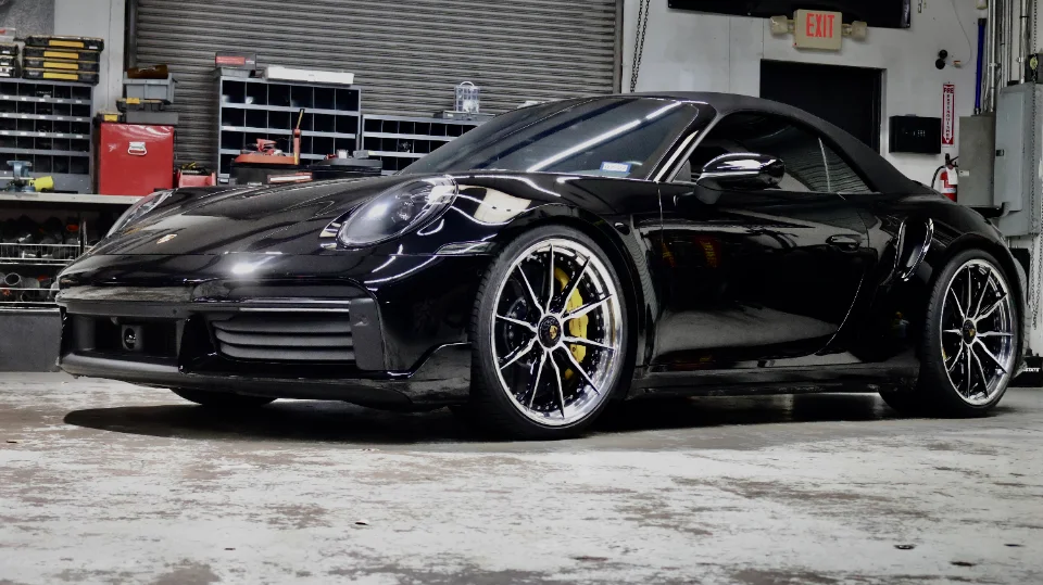 Black Porsche 911 convertible with aftermarket wheels and yellow brake calipers parked inside a performance tuning shop.