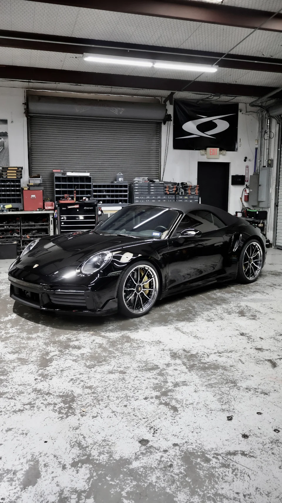 A sleek black Porsche 911 convertible with custom wheels parked inside a well-lit performance tuning shop.