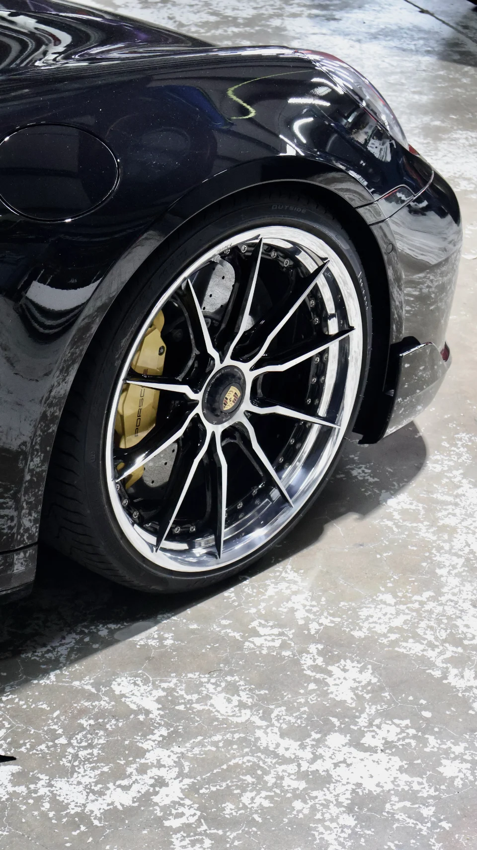 Close-up detail of a black Porsche's custom multi-spoke wheel with a polished lip and gold brake caliper.
