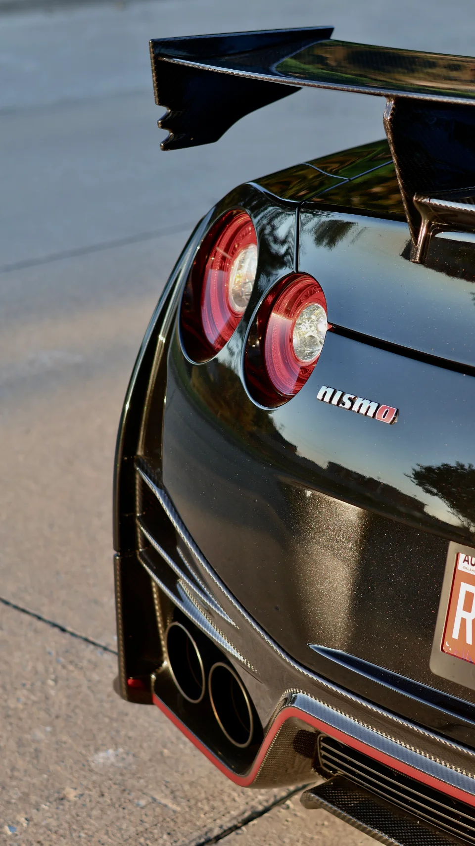 A close-up of the rear of a black Nissan GT-R Nismo, showcasing its distinctive taillights, large carbon fiber rear wing, and quad exhaust tips.