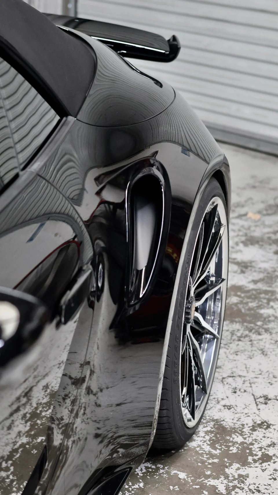 Close-up of a highly polished black Porsche with chrome multi-spoke wheels and a side air intake, showcasing the car's sleek design.