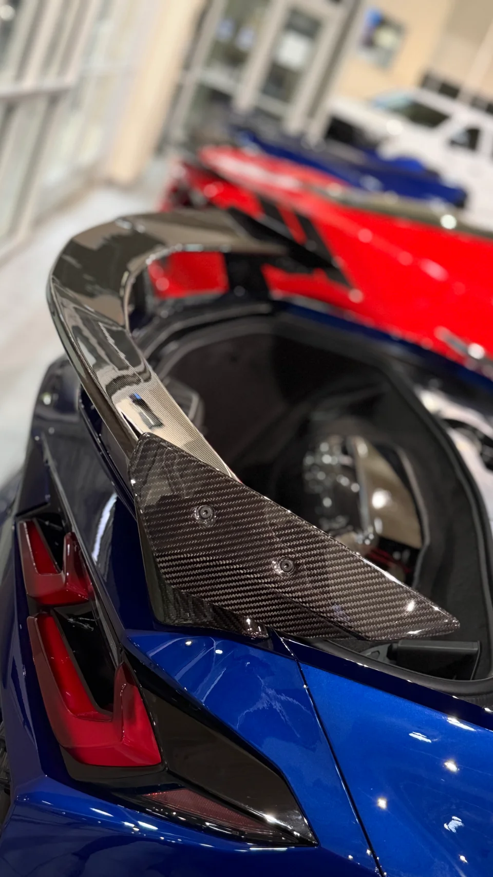 Close-up of a blue Chevrolet Corvette C8's rear with a carbon fiber high-wing spoiler in a showroom setting.