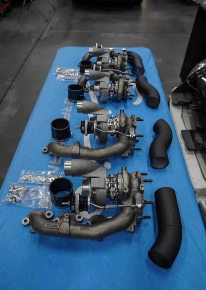 Multiple aftermarket turbochargers, exhaust manifolds, and boost piping laid out on a blue table.