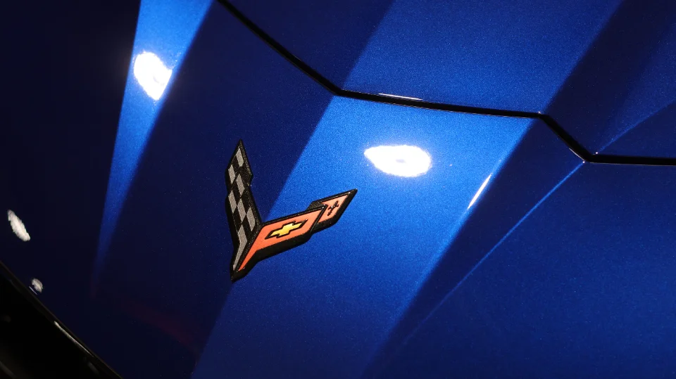 A close-up detail shot of a blue Chevrolet Corvette's hood featuring the iconic Corvette crossed flags emblem.