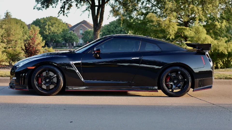 Black Nissan GT-R with aftermarket wheels, red brake calipers, and a large rear wing parked on a street.