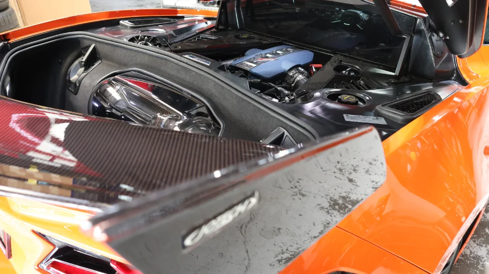 Close-up of an orange C8 Corvette engine bay with a carbon fiber rear wing and aftermarket intake components.