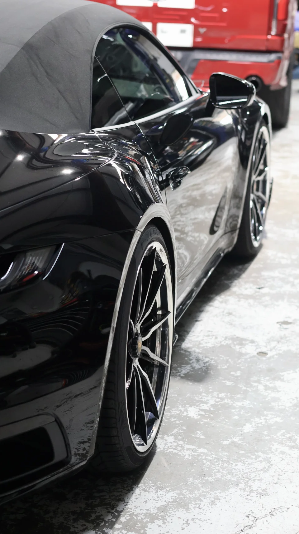 A sleek black Porsche convertible with custom multi-spoke wheels parked on a polished concrete floor.