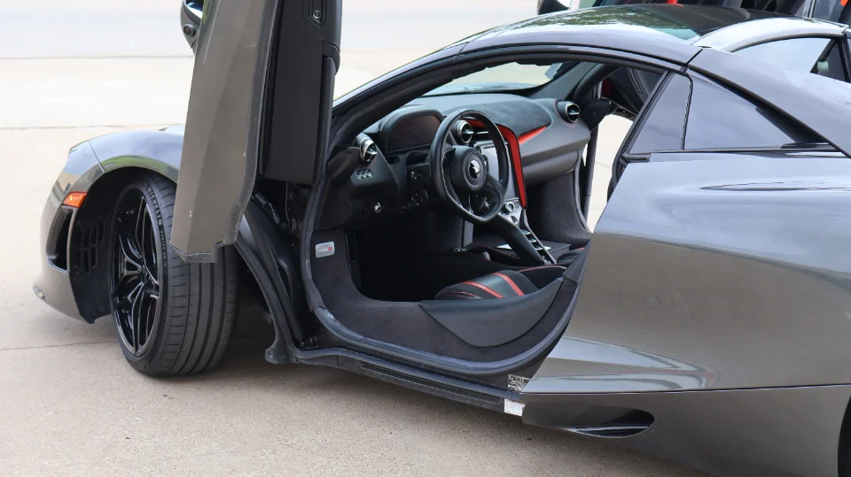 Grey McLaren 720S supercar with butterfly doors open, showcasing the black and red interior and custom wheels.