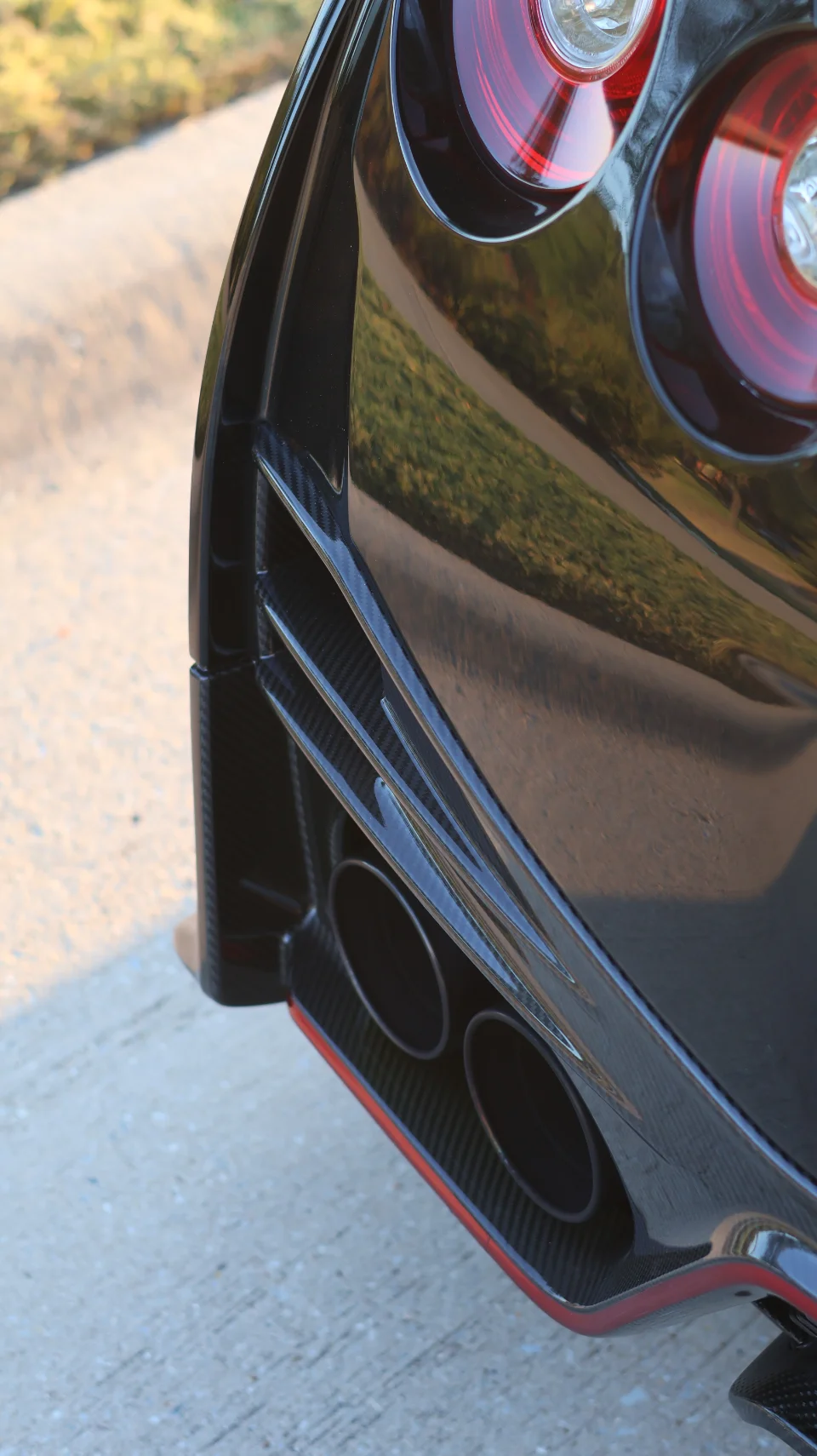 A close-up detail shot of a black Nissan GT-R's carbon fiber rear diffuser, quad exhaust tips, and round taillights.