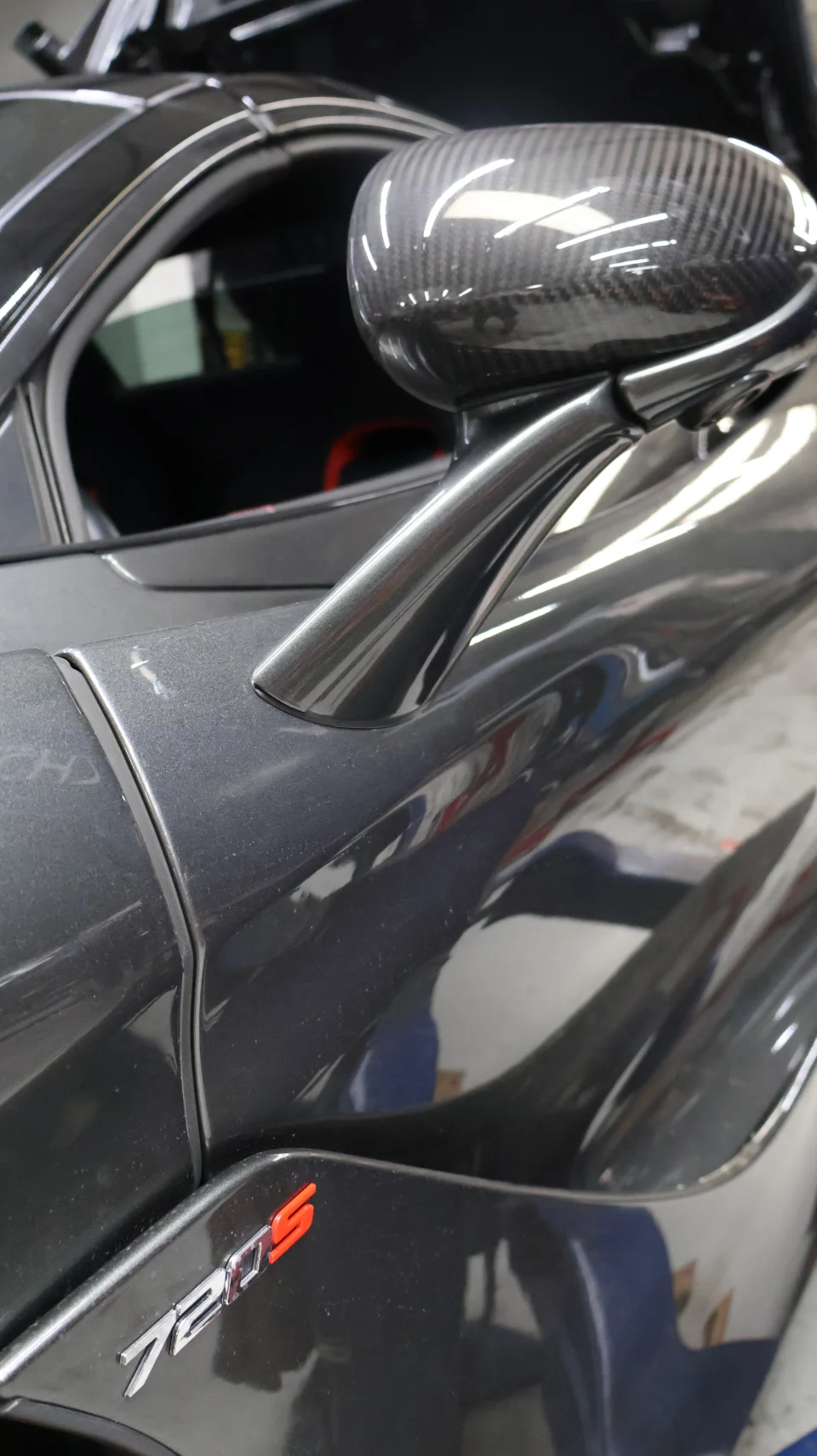 Close-up detail of a grey McLaren 720S with a carbon fiber side mirror and '720S' badging.
